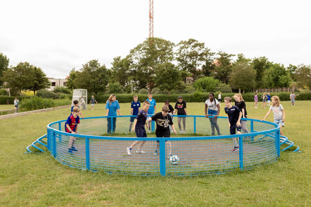 4 jongens spelen voetbal in pannakooi, jongeren supporteren rond pannakooi