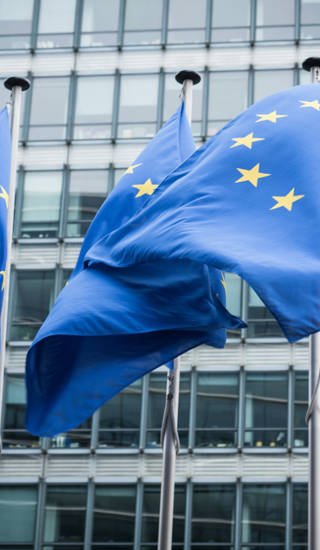 Drie Europese vlaggen wapperen voor het gebouw van de Europese Unie in Brussel