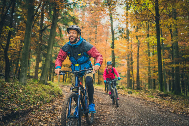 Smiling young adult black man enjoying sport with friends in nature. Adventure trip in colourful autumn forest, active lifestyle concept.