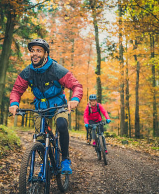 Smiling young adult black man enjoying sport with friends in nature. Adventure trip in colourful autumn forest, active lifestyle concept.