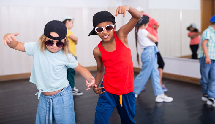 Meisje en jongen met pet en zonnebril tijdens groepsles in dansstudio