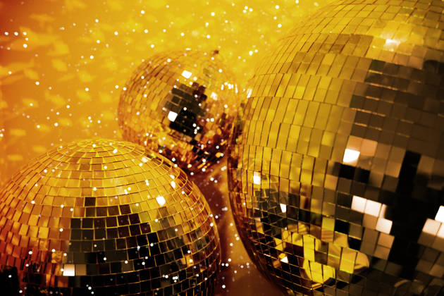 Gold colored party disco ball baubles on bright yellow background.