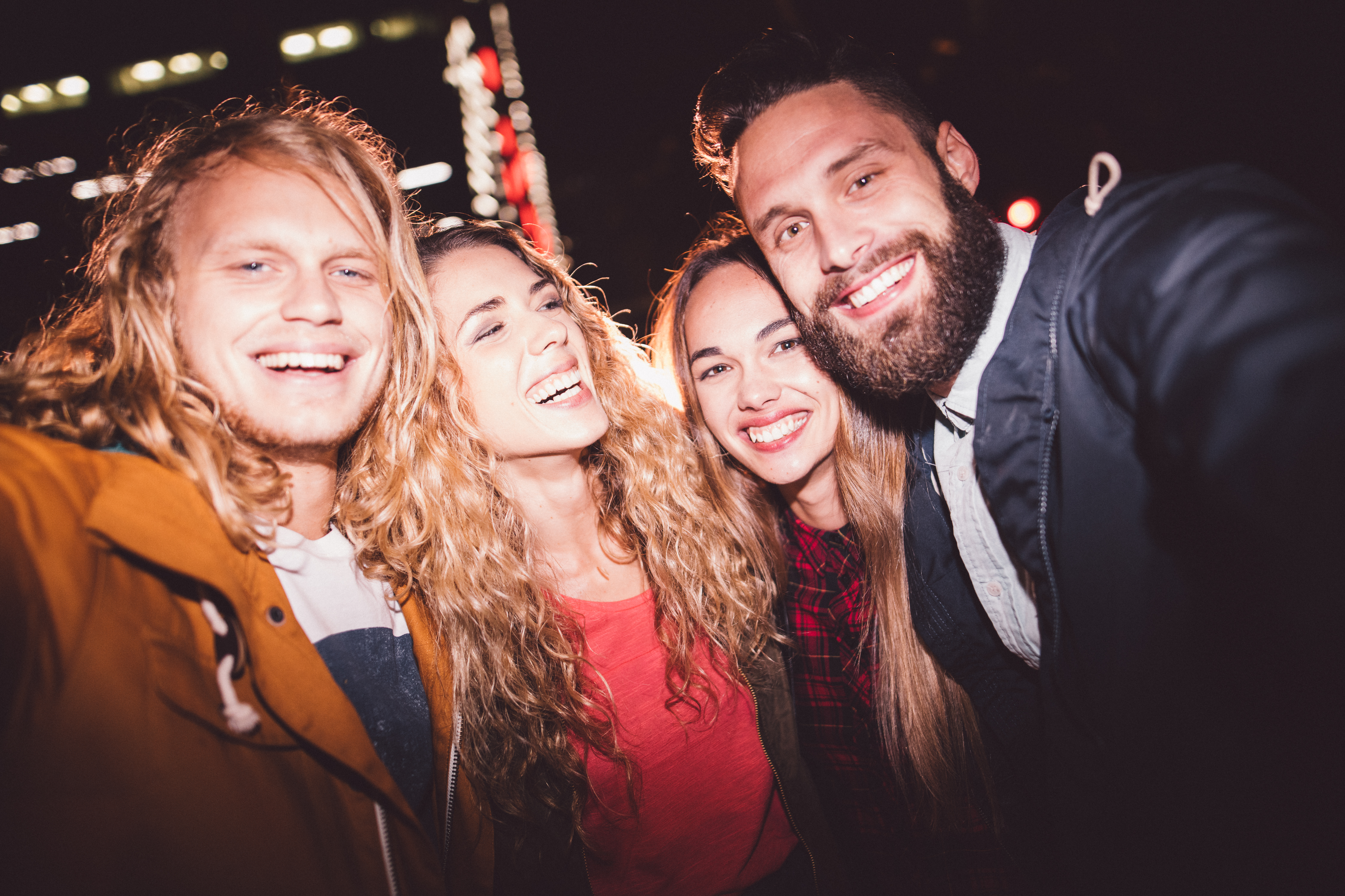 Hipster teen friends taking a seflie with a smartphone smiling and embracing each other with city light in the background