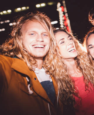 Hipster teen friends taking a seflie with a smartphone smiling and embracing each other with city light in the background