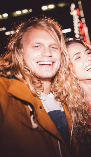 Hipster teen friends taking a seflie with a smartphone smiling and embracing each other with city light in the background