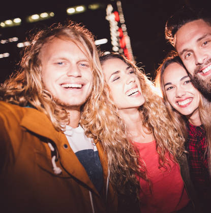 Hipster teen friends taking a seflie with a smartphone smiling and embracing each other with city light in the background