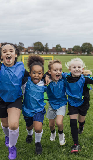 Front view of a small group of boys and girls wearing sports clothing, football boots and a sports bib on a football pitch in the North East of England. They are at football training where they are doing different football training drills. They are running and celebrating with their arms around each other in front of a football goal while smiling and looking at the camera.
Videos are available for this scenario.