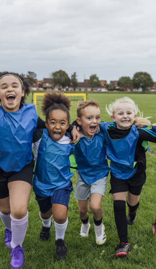 Front view of a small group of boys and girls wearing sports clothing, football boots and a sports bib on a football pitch in the North East of England. They are at football training where they are doing different football training drills. They are running and celebrating with their arms around each other in front of a football goal while smiling and looking at the camera.
Videos are available for this scenario.