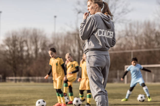 Jonge vrouwelijke voetbalcoach met haar meisjesteam blaast op fluitje