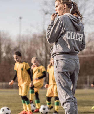 Jonge vrouwelijke voetbalcoach met haar meisjesteam blaast op fluitje