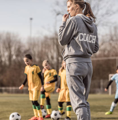 Jonge vrouwelijke voetbalcoach met haar meisjesteam blaast op fluitje