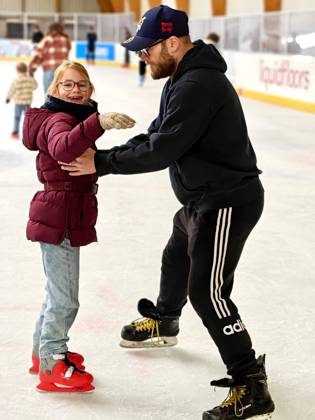 Jong meisje op schaatsen wordt begeleid op het ijs door trainer of coach