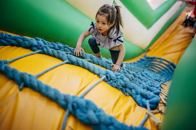 Cute little girl playing in climbing up inflatable bouncy castle in amusement park.