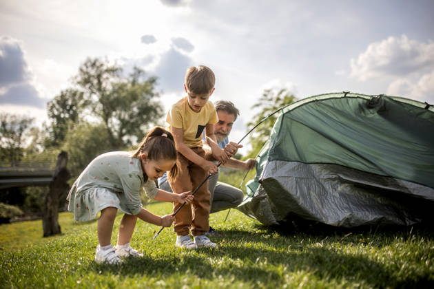 a multigenerational family is camping in a park by the river and setting up a tent