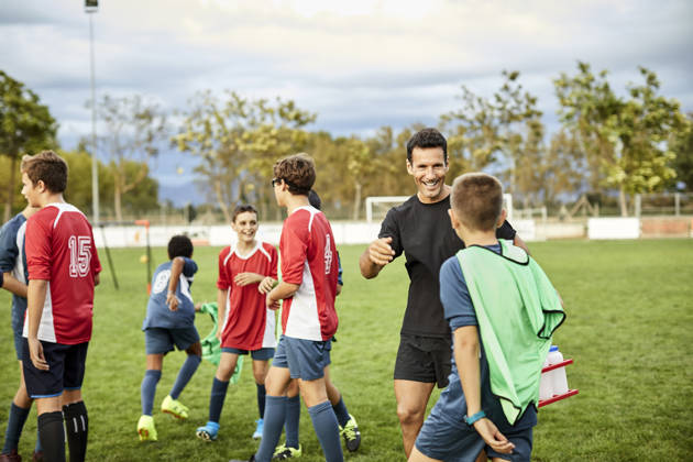 Lachende trainer en tieners op voetbalveld