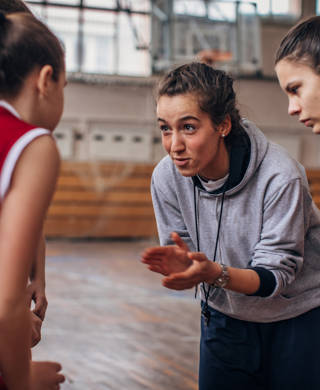 Vrouwelijke basketbalcoach in het midden van meisjesteam in sporthal