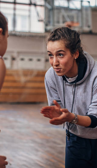 Vrouwelijke basketbalcoach in het midden van meisjesteam in sporthal