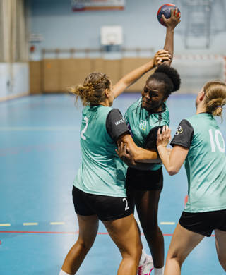 Handbalspeelster probeert bal te gooien terwijl tegenspeelsters dat verhinderen
