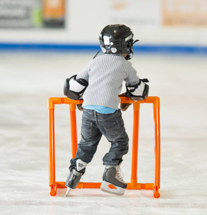 Kleine jongen met schaatsen aan oefent met hulprekje