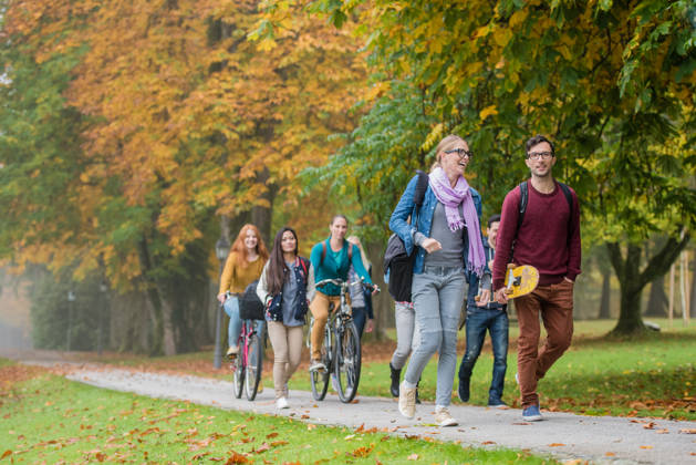 University students walking and cycling on footpath in campus.