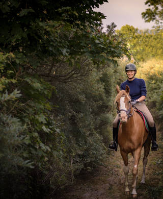 Portrait of a young woman who is riding her tan coloured Arabian horse through the woods on her way to the beach. Photographed the island of Møn in Denmark. Colour, horizontal with some copy space.