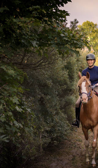Portrait of a young woman who is riding her tan coloured Arabian horse through the woods on her way to the beach. Photographed the island of Møn in Denmark. Colour, horizontal with some copy space.