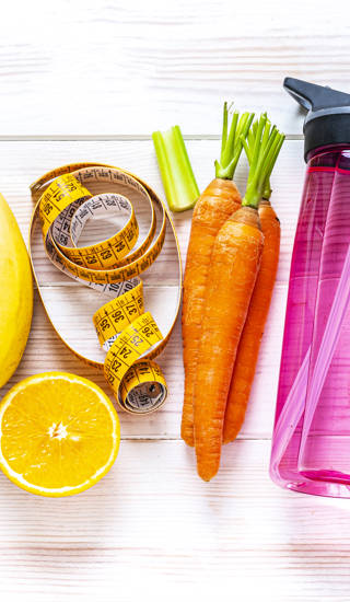 Exercising and healthy eating concept: overhead view of rainbow colored dumbbells, jump rope, water bottle, towel, tape measure and healthy fresh organic vegetables, fruits and nuts arranged side by side on white background. The composition includes spinach, tomato, carrot, banana, apple, blueberry, almonds, orange, celery, grape among others. High resolution 29Mp panoramic format studio digital capture taken with SONY A7rII and Zeiss Batis 40mm F2.0 CF lens