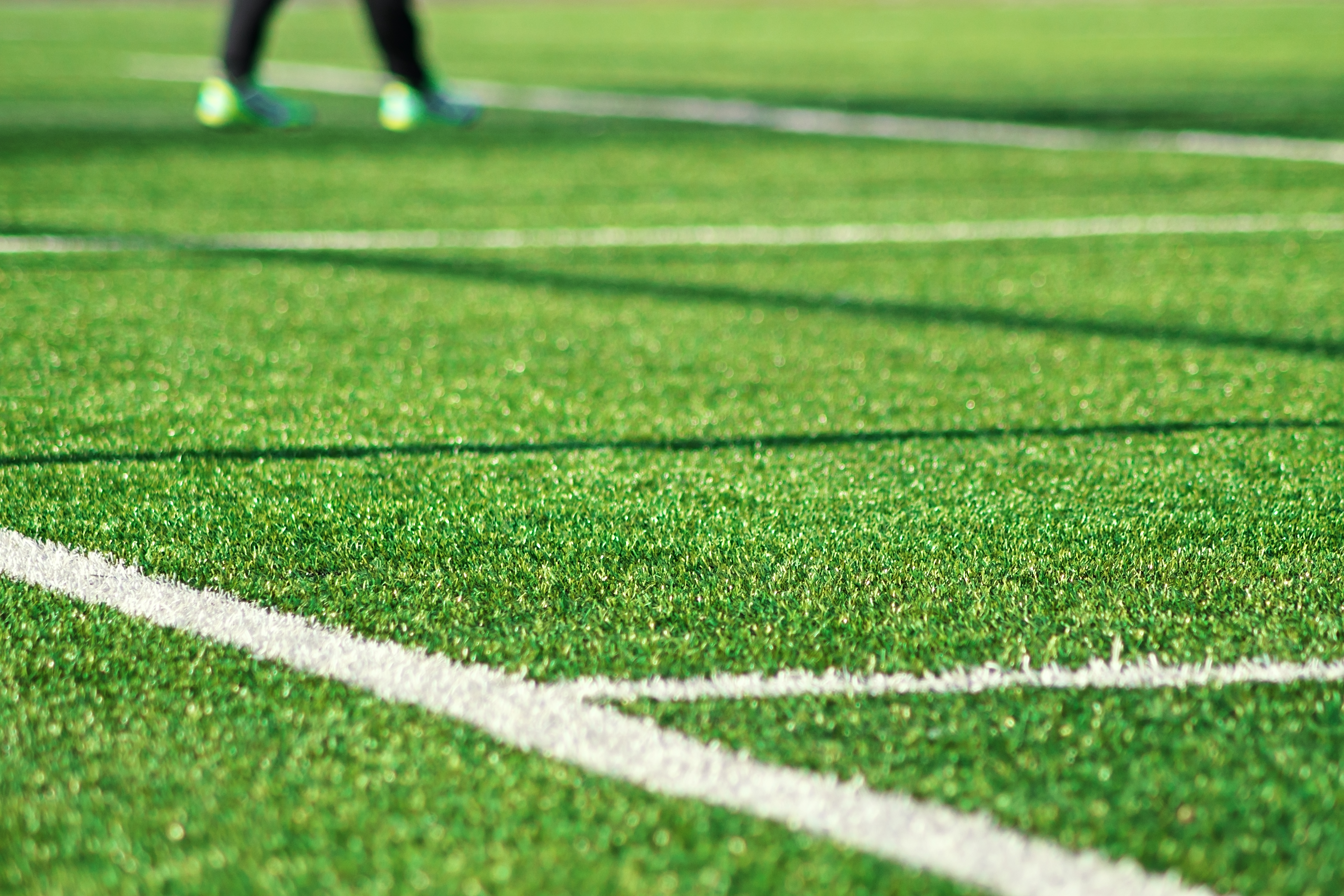 Artificial green grass  with white stripe of soccer field. White line on green grass a field of play. Fake Grass used on sports fields for soccer and football. Closed-up of artificial grass background.
