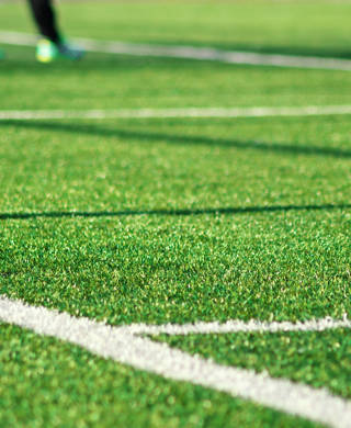 Artificial green grass with white stripe of soccer field. White line on green grass a field of play. Fake Grass used on sports fields for soccer and football. Closed-up of artificial grass background.