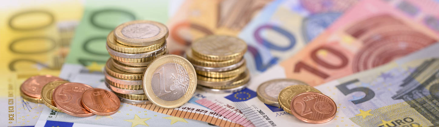 many banknotes of European currency laying under stacked coins