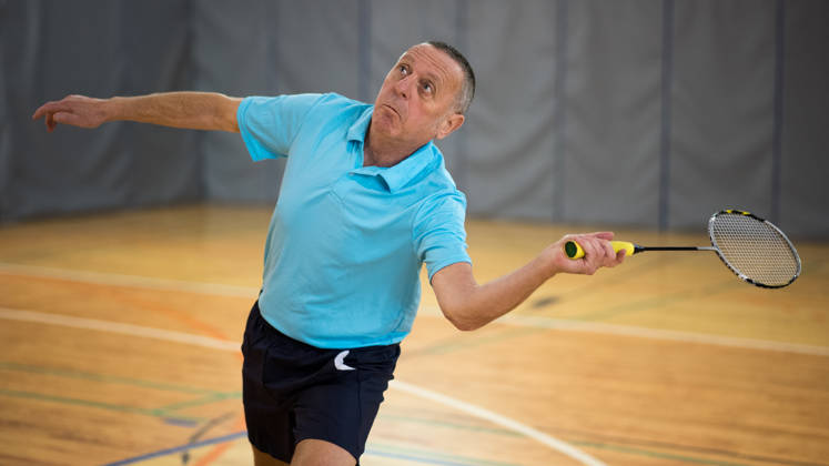 Senior man hitting shuttlecock with badminton racquet in court.
