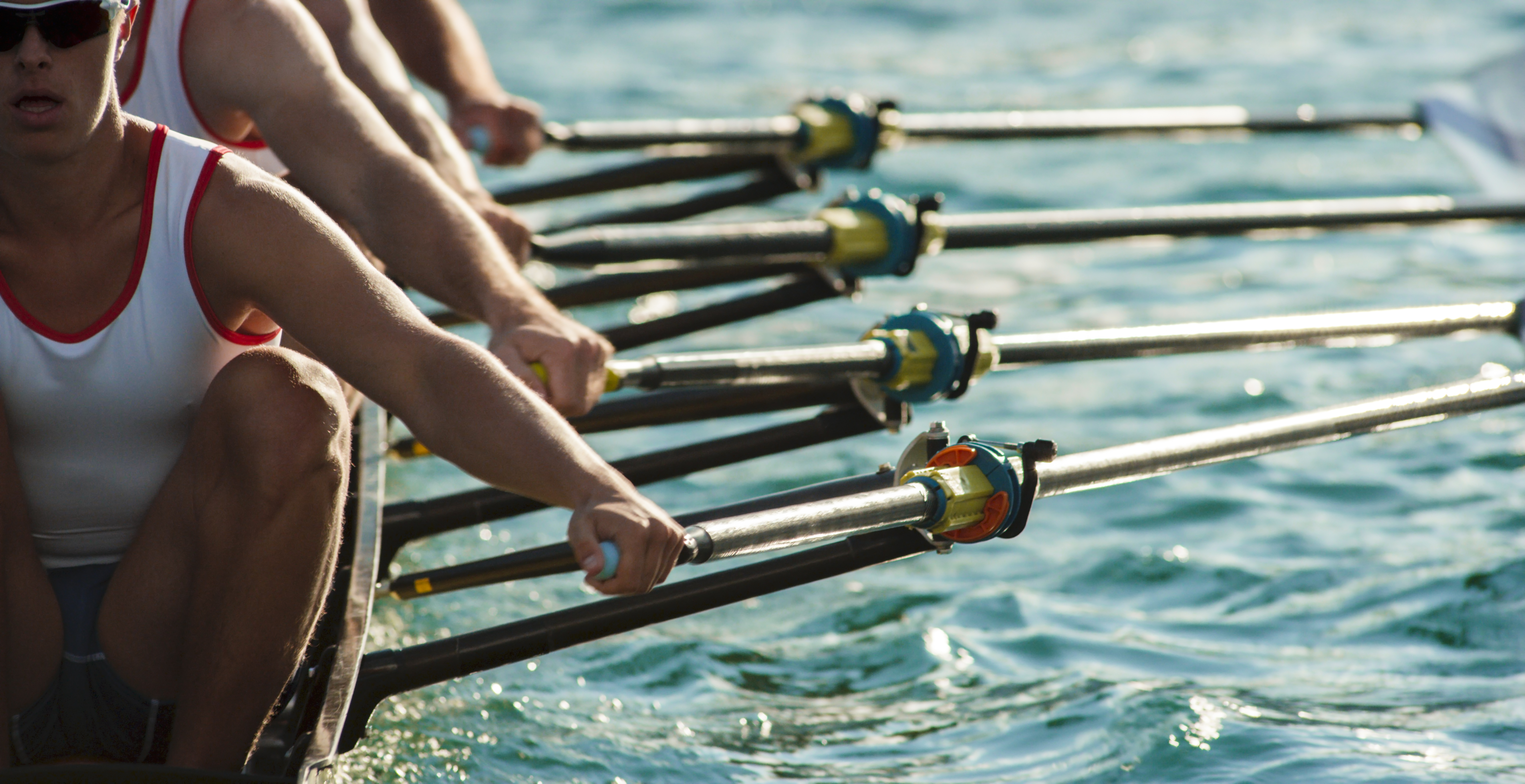 Four male rowers rowing across lake in late afternoon.
