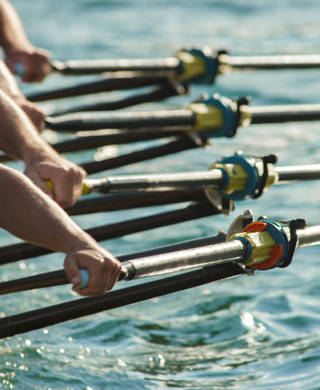 Four male rowers rowing across lake in late afternoon.