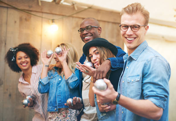 Group of smiling beautiful young people men and women in casual wear standing indoors and posing to camera holding petanque metal balls, laughing