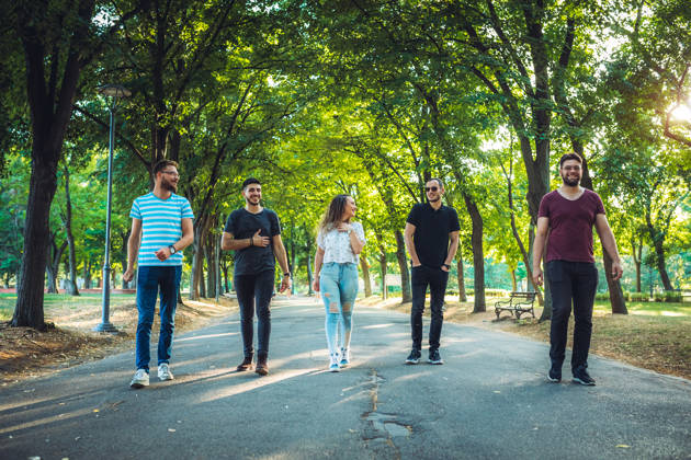Group of young caucasian smiling friends having a walk in a public park on a sunny day together.