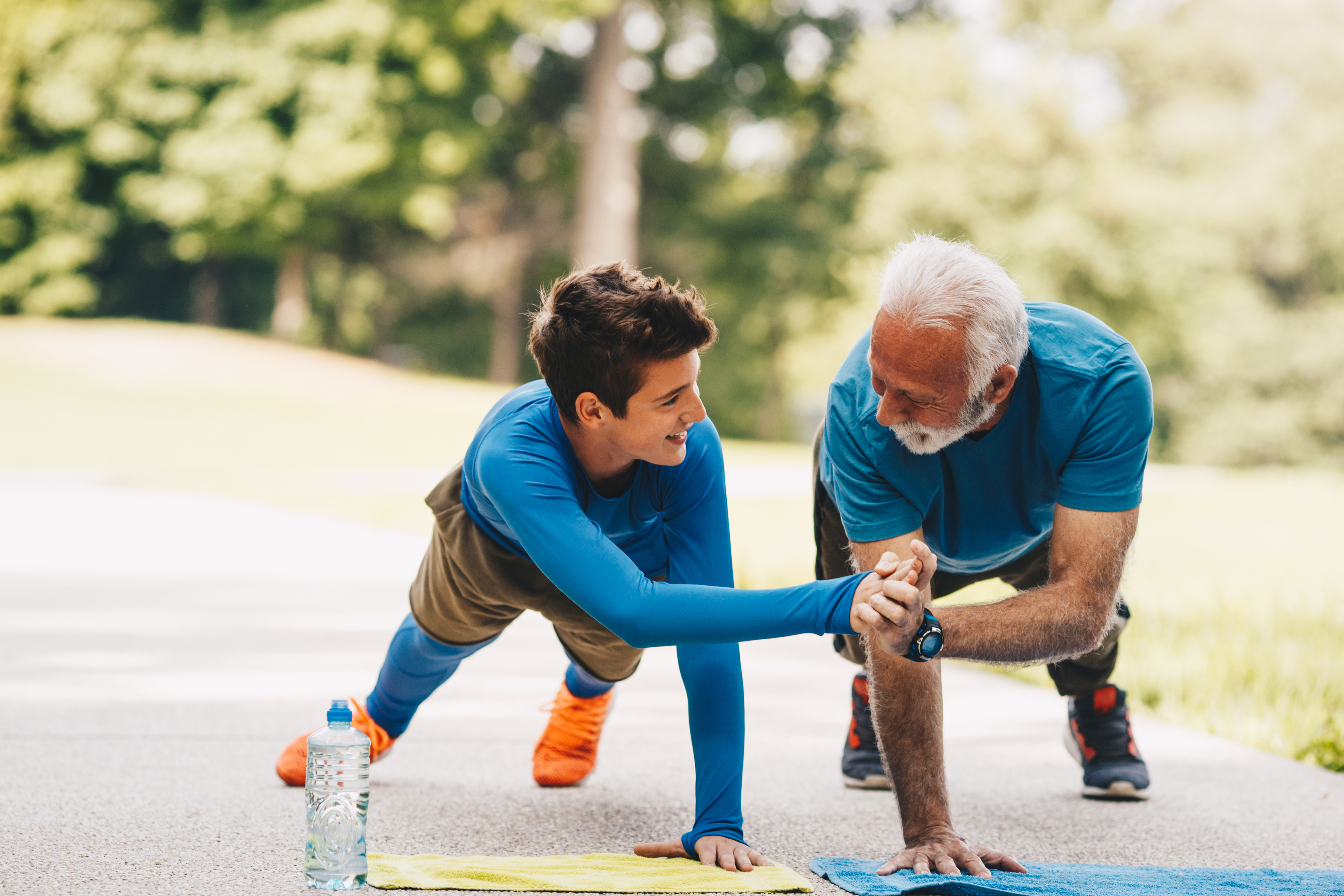 Granddad is doing exercises with his grandson in park. They are now finishing series of push ups. They had enough for today. Both of them are proud of themselves and progress they made today.