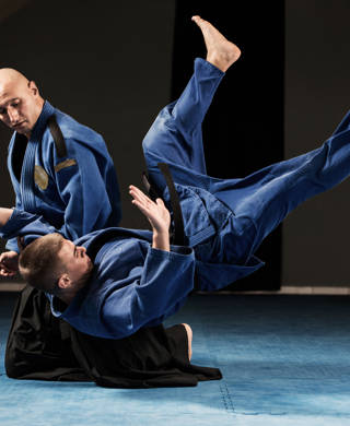 Twee mannen in blauwe kimono, ene valt met rug op de grond
