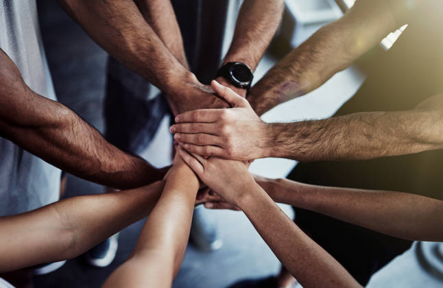 Cropped shot of a group of fit people joining their hands in unity at the gym
