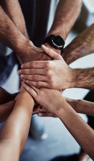 Cropped shot of a group of fit people joining their hands in unity at the gym