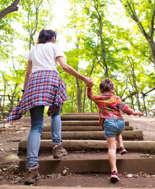 Mother and daughter are up the stairs in the woods hand in hand