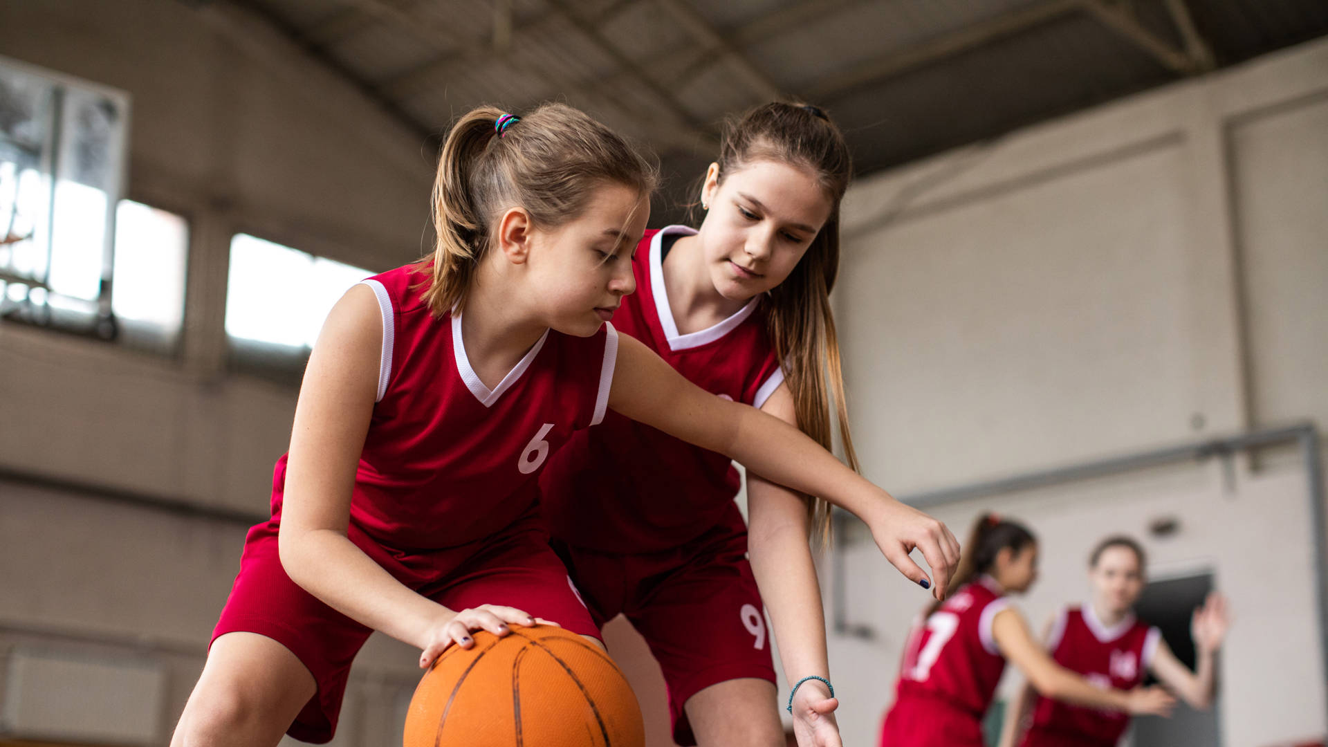 Female basketball team playing match in school gym, dribbling ball on sport filed