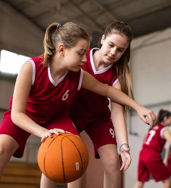 Female basketball team playing match in school gym, dribbling ball on sport filed