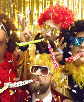 Multiethnic friends company in carnival wear blowing in party pipes have fun under confetti rain. Headshot portrait on nightclub sparkling background. Festive atmosphere, birthday, corporate event