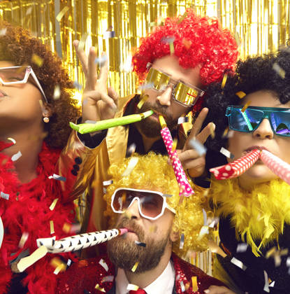 Multiethnic friends company in carnival wear blowing in party pipes have fun under confetti rain. Headshot portrait on nightclub sparkling background. Festive atmosphere, birthday, corporate event