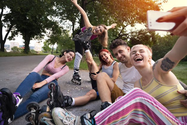A small group of young Caucasian skaters using a smartphone while taking selfies in the park.