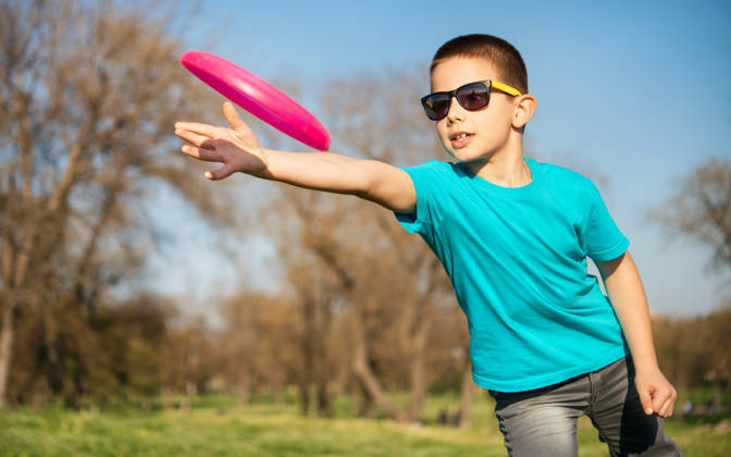 Jonge jongen met zonnebril speelt met rose frisbee in het park