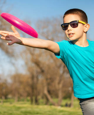 Jonge jongen met zonnebril speelt met rose frisbee in het park