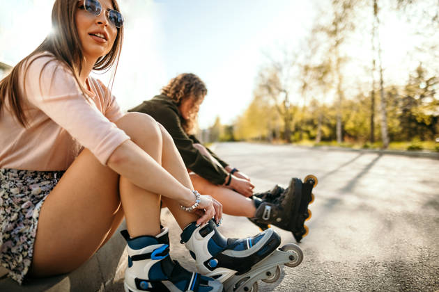 Young female skater sitting in the park and ties her rollers