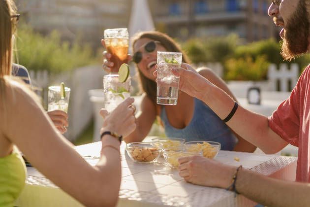 Happy hour toasting. Young friends clinking with fresh mojitos sitting in a counter restaurant and taking aperitif in the summer. Friendship and togetherness concept