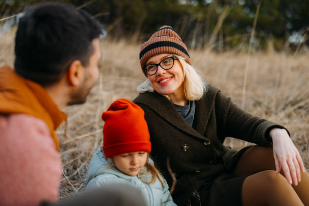 A family of three enjoys a cozy moment outdoors during an autumn vacation in the mountains. The scene captures warmth and togetherness surrounded by nature.